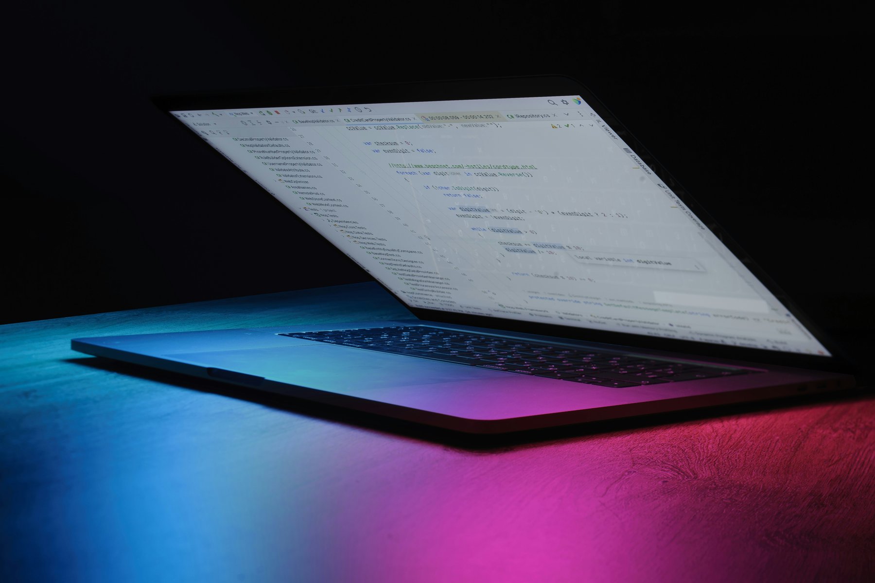 Laptop screen showing code in a dark room with blue and magenta lighting